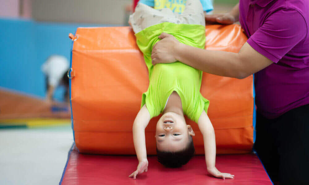 A smiling little girls tryig to hold on to a gym ball.