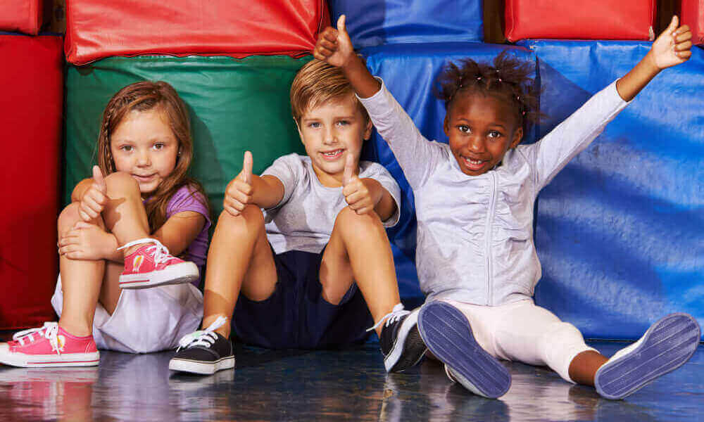 Happy group of kids in preschool gym holding their thumbs up.